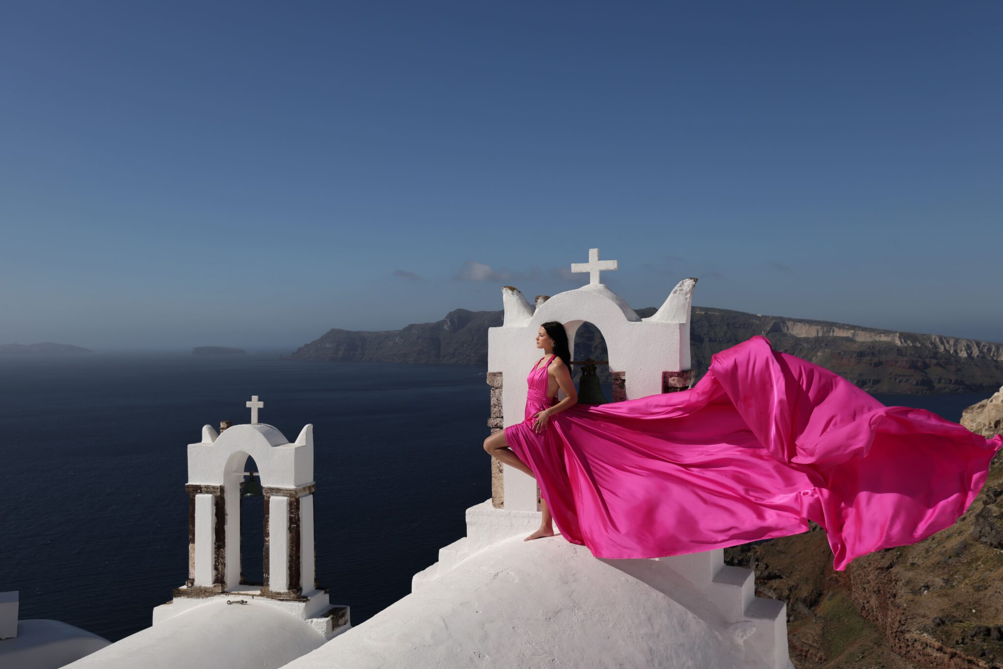 Flying dress photoshoot near the white architecture and blue domes of Oia, Santorini