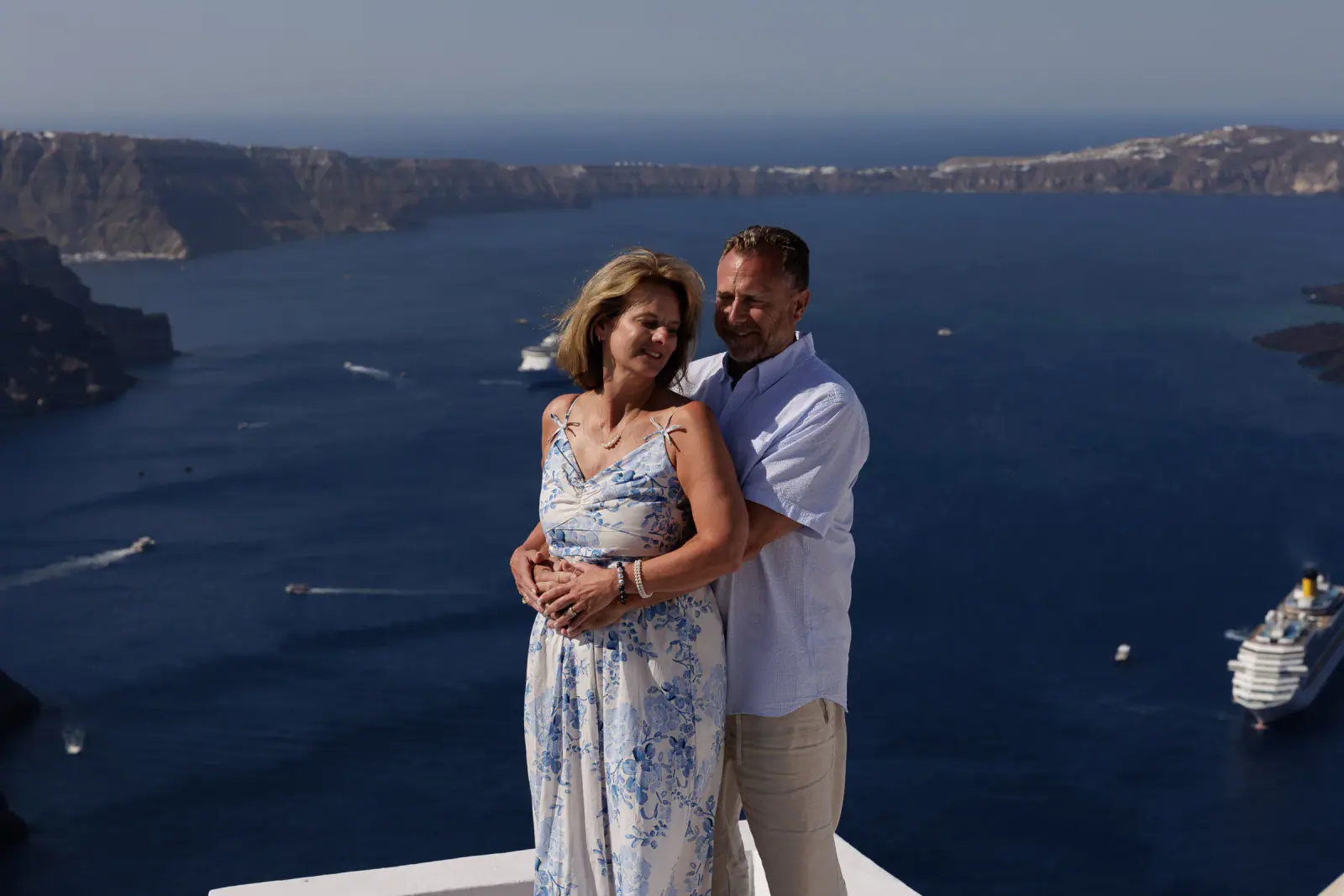 Couple embracing above the caldera with a cruise ship below
