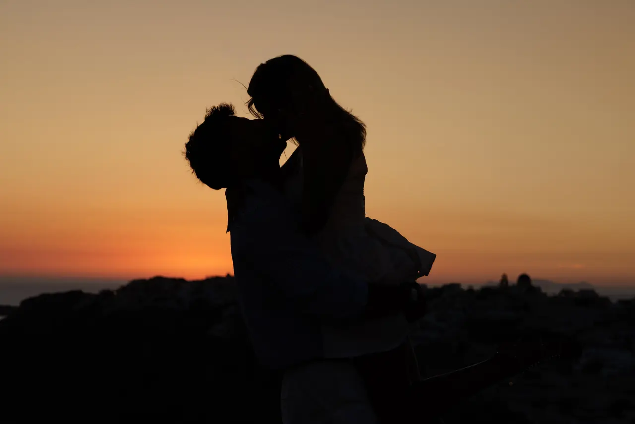 Charlie and Kayce silhouetted together against the orange Santorini sunset
